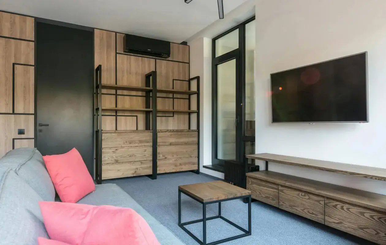Moderne woonkamer met grijze bank, houten meubels en een tv. De airco leidingen zijn netjes weggewerkt in het design.