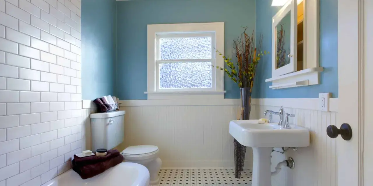Badkamer met witte tegels, blauwe muur, toilet, wastafel en een spiegel die verven een frisse look geeft.