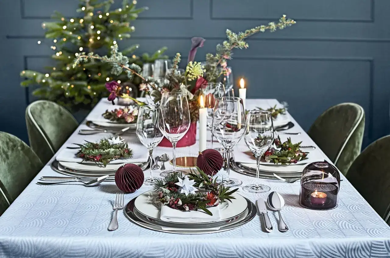 Een feestelijk gedekte tafel met kerstversiering, glazen, kaarsen en een kerstboom op de achtergrond.