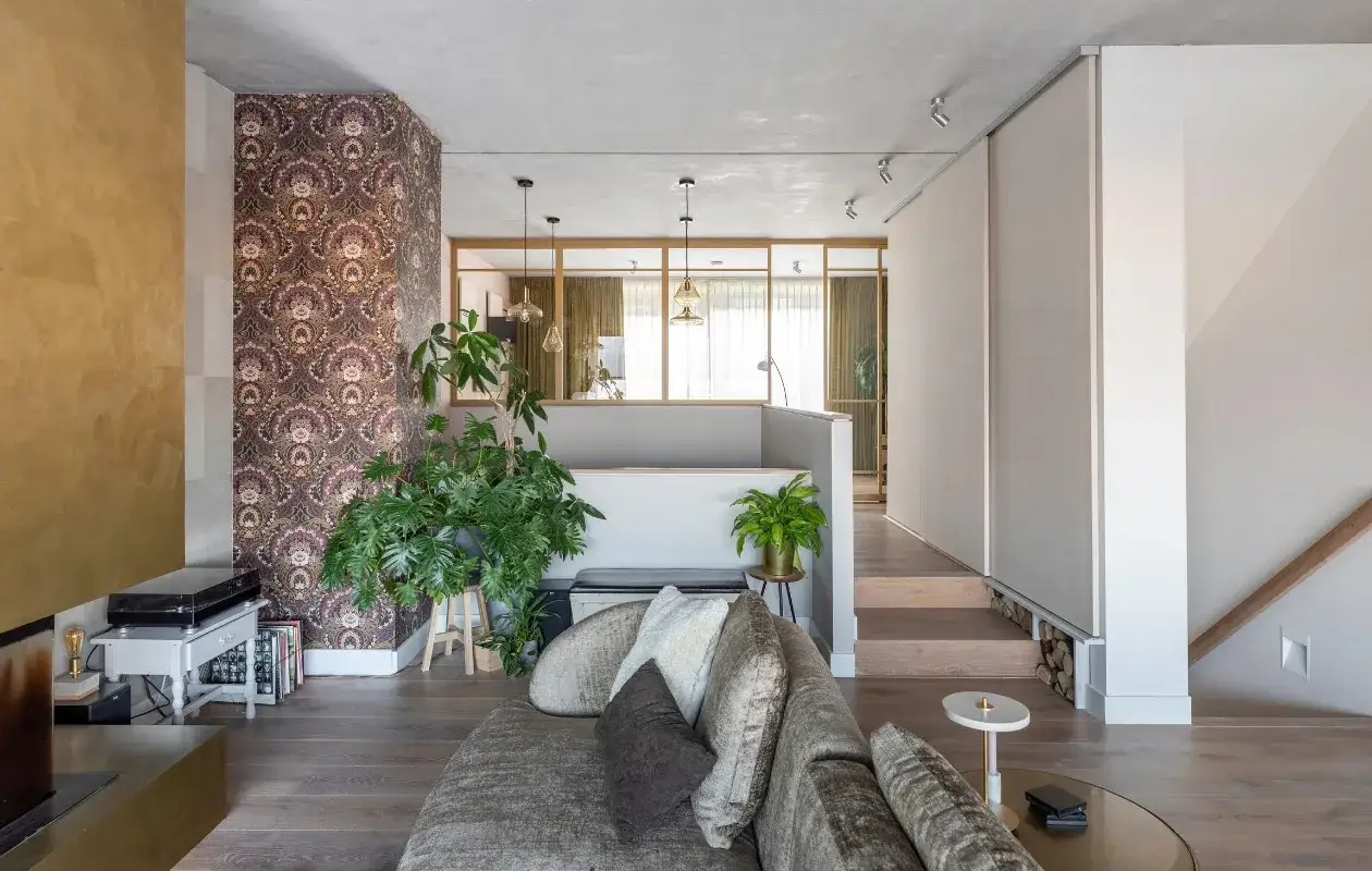 Luxe split level woning met opvallend behang, veel groen en een comfortabele bank. De trap leidt naar een hogere verdieping.