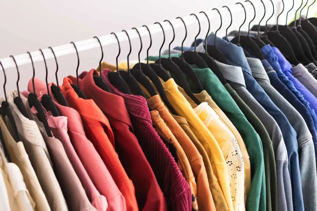 Een regenboog aan kleding hangt aan zwarte hangers. Het is een kleurrijke kledingkast opruimen, van zachtroze tot diepblauw.