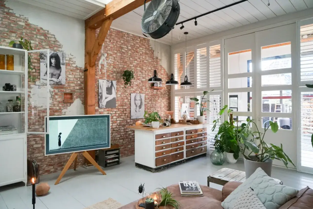 Een woonkamer met bakstenen muur, vintage meubels en veel planten. De sfeer is warm en industrieel, wat laat zien wat is vintage.