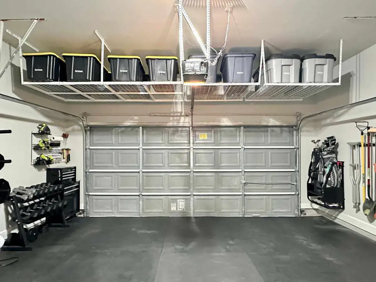 Slimme opbergoplossingen voor een kleine garage inrichten: rekken aan het plafond met bakken, dumbbells, gereedschap en golfclubs netjes opgeborgen.