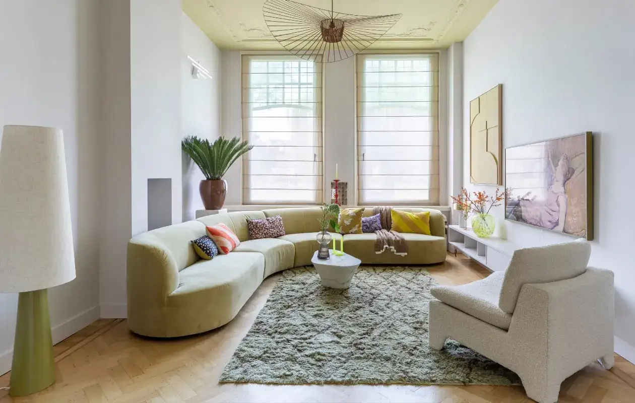 Een lichte woonkamer met een comfortabele, gebogen bank, perfect voor alleen wonen. Een grote vloerlamp en een zacht tapijt creëren een knusse sfeer.