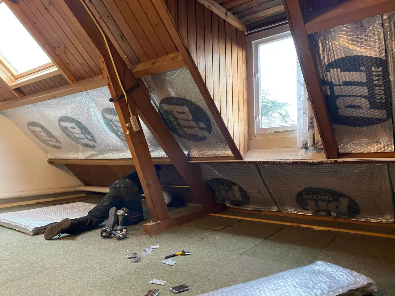 Man isoleert een zolder met reflecterend materiaal om warmte in huis te houden.