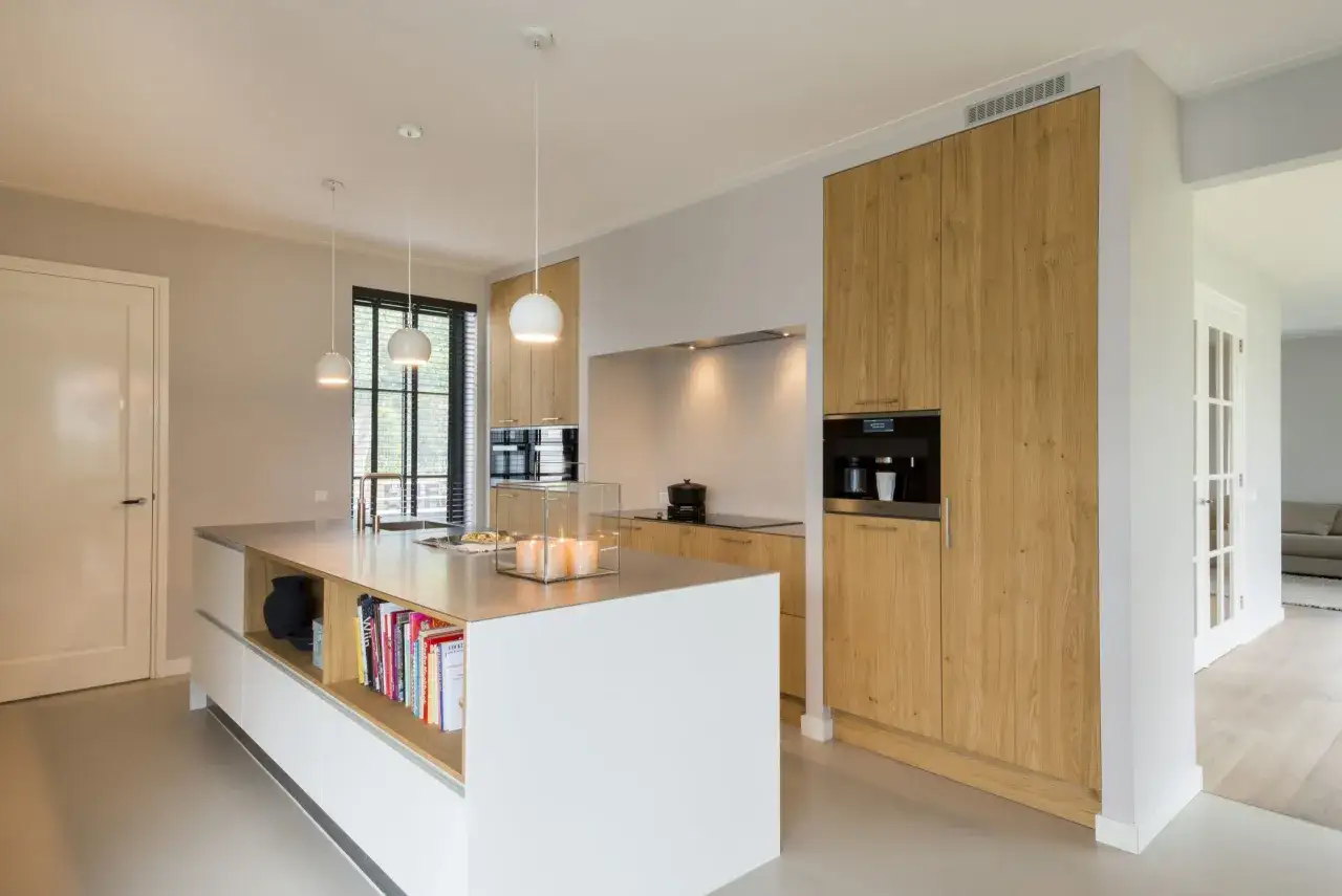 Moderne nis keuken met houten kasten, een kookeiland met boeken en een ingebouwde koffiemachine.