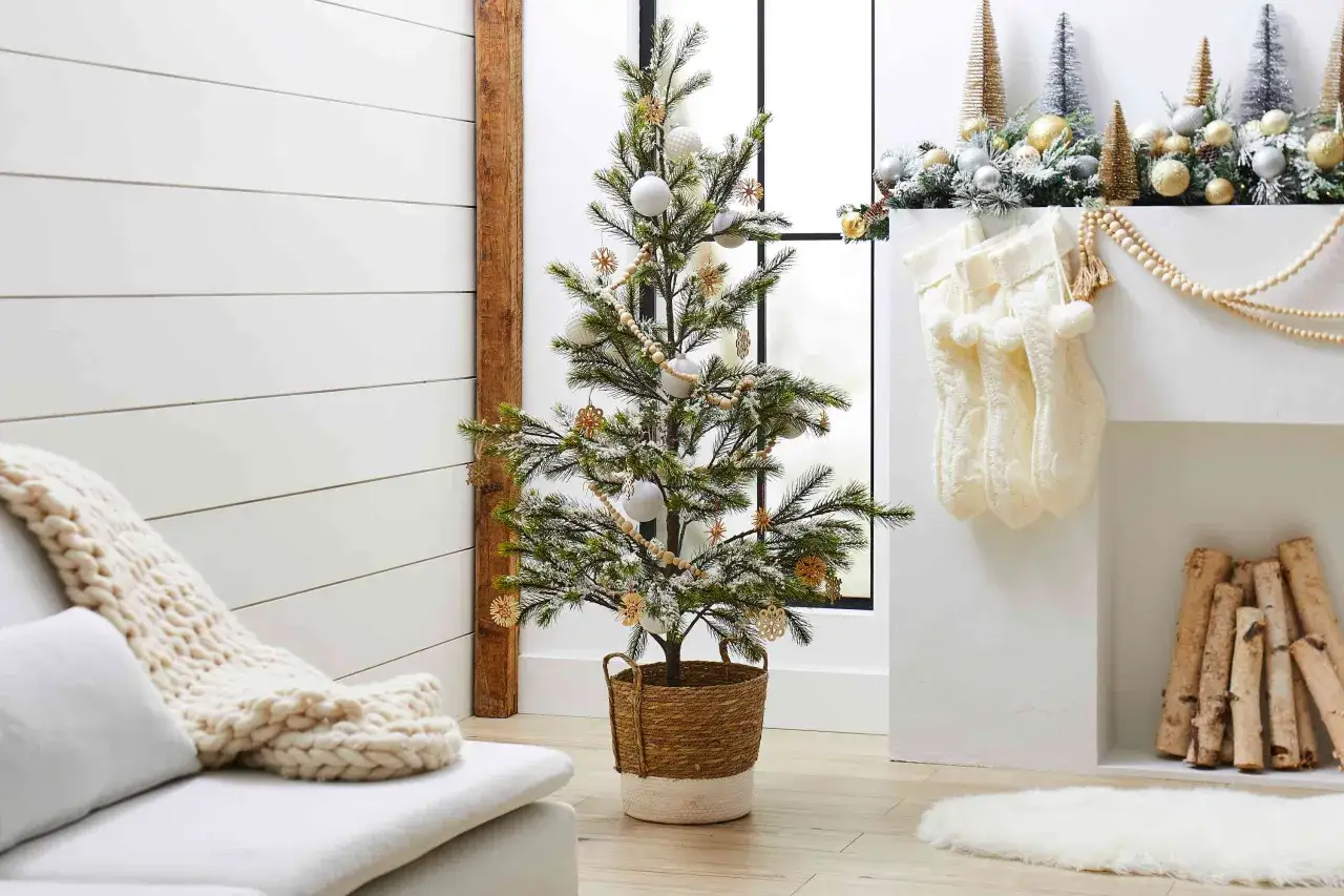 Een sfeervolle kerstboom in Scandinavische stijl, versierd met witte ballen en houten ornamenten, staat in een mand.
