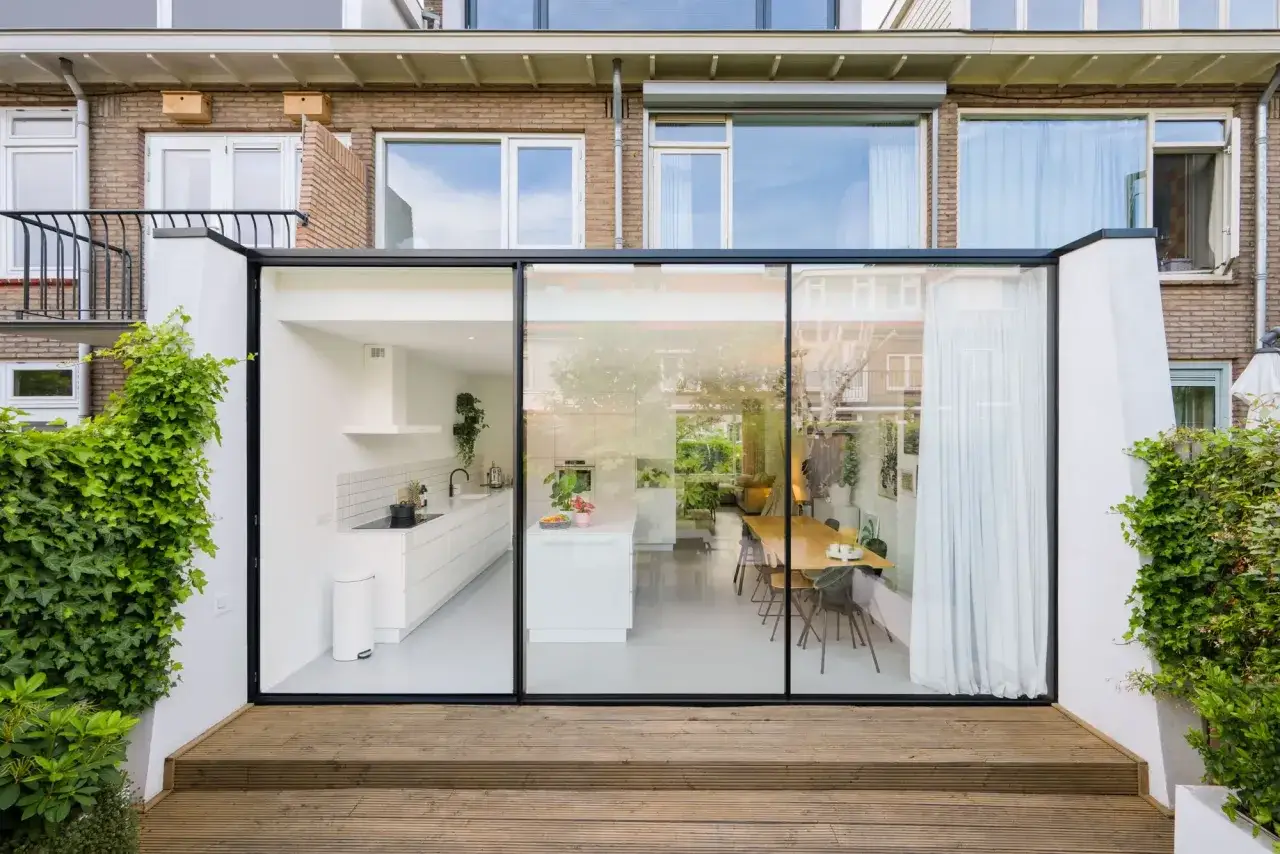 Moderne aanbouw met glazen pui toont strakke witte keuken en eethoek. Goede huis verbouwen tips voor licht en ruimte.
