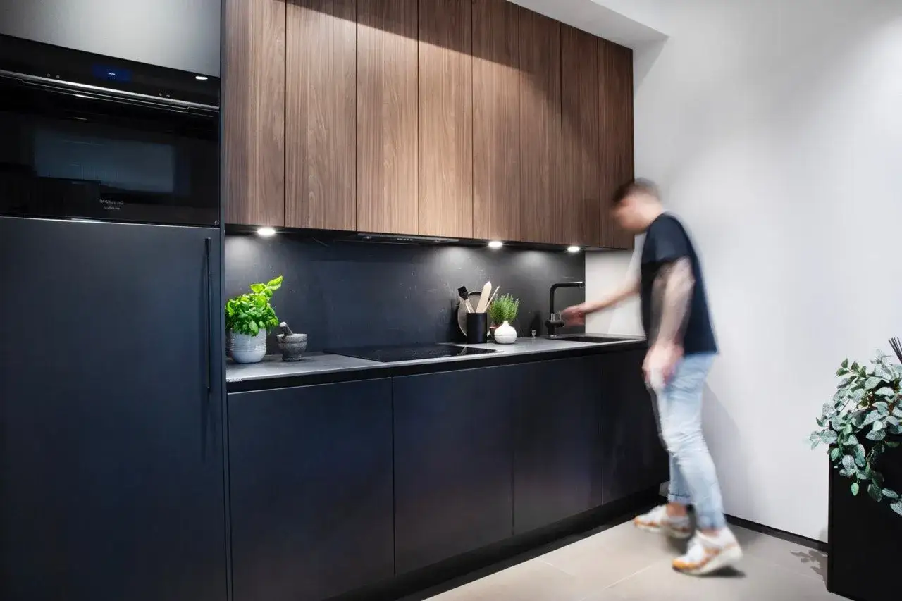 Moderne donker hout keuken met zwarte kasten en een man die de kraan bedient.