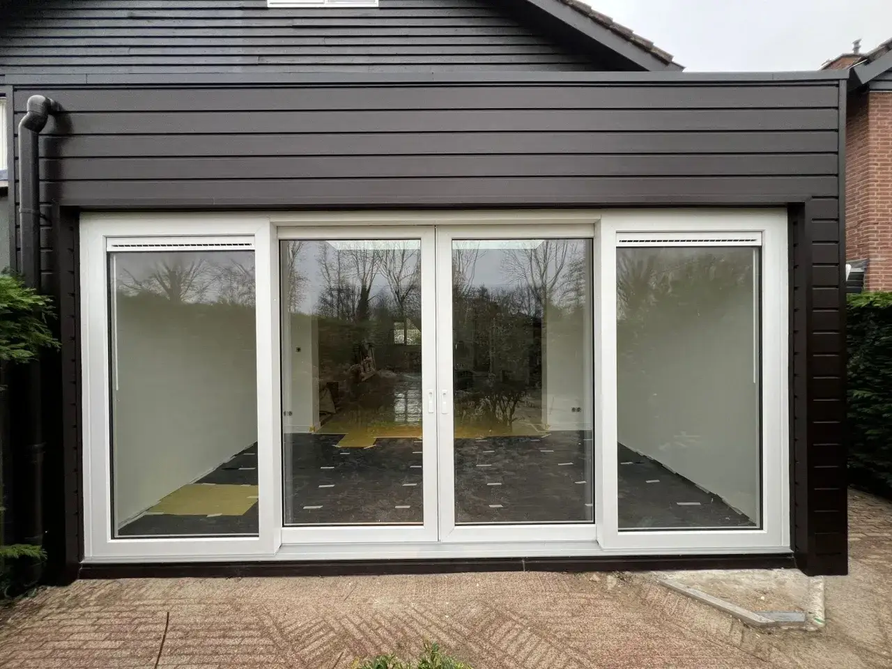Moderne prefab woning met grote glazen schuifpui, donkergrijs gevelbekleding en een dakgoot.