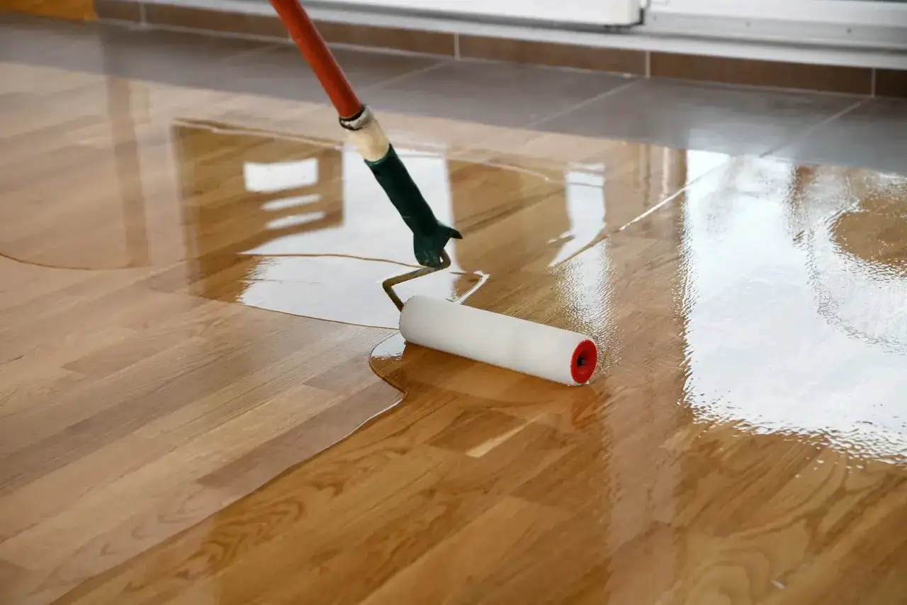 Een roller brengt een laklaag aan op een houten vloer, waardoor de bestaande krassen in het gelakte hout verdwijnen en de vloer weer glanst.