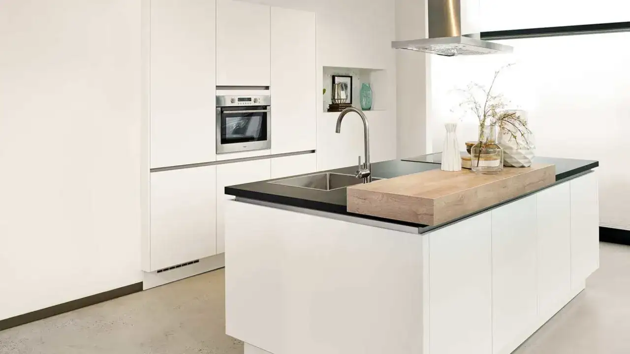 Een strakke, minimalistische keuken met witte kasten, een ingebouwde oven en een eiland met spoelbak en houten snijplank.