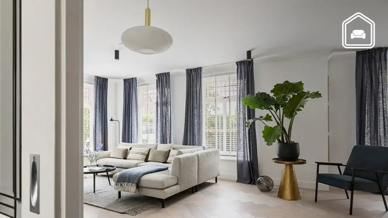 Een lichte woonkamer met een grote hoekbank, donkerblauwe gordijnen en een plant. Een inspiratie voor ontspullen in 52 weken.