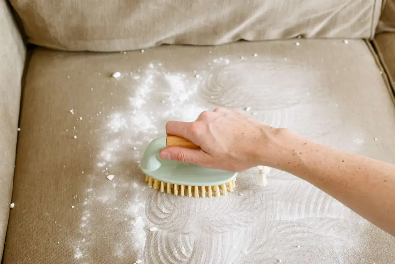 Hand met borstel maakt de bank schoon met poeder, zodat de bank lekker laten ruiken.