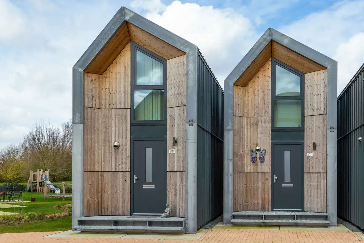 Moderne, houten tiny huisjes met schuine daken. Een speelplaats is zichtbaar in de achtergrond.