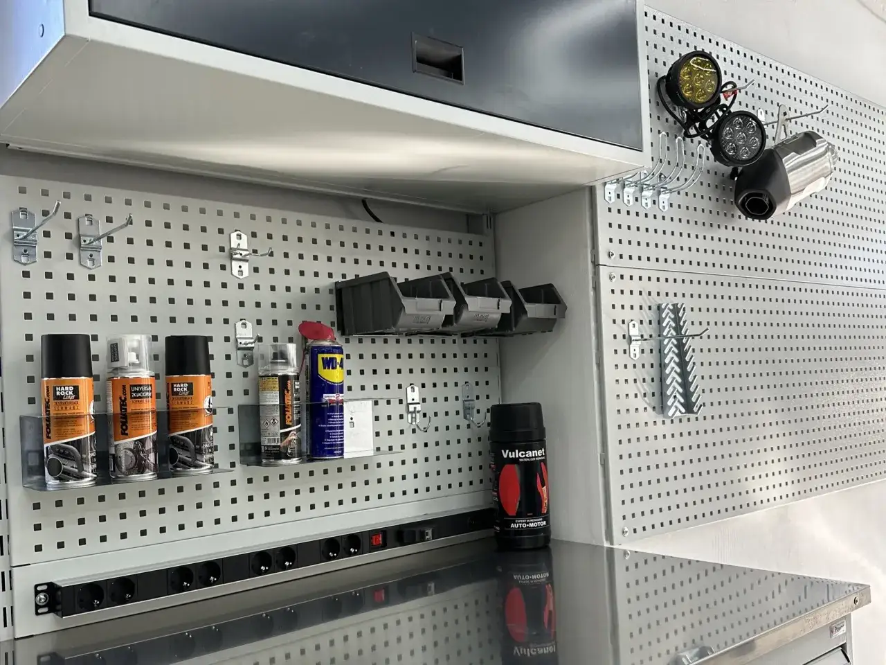 Een georganiseerde garagebox met spuitbussen, lampen en een uitlaat op een pegboard. Ideaal voor garagebox inrichten.