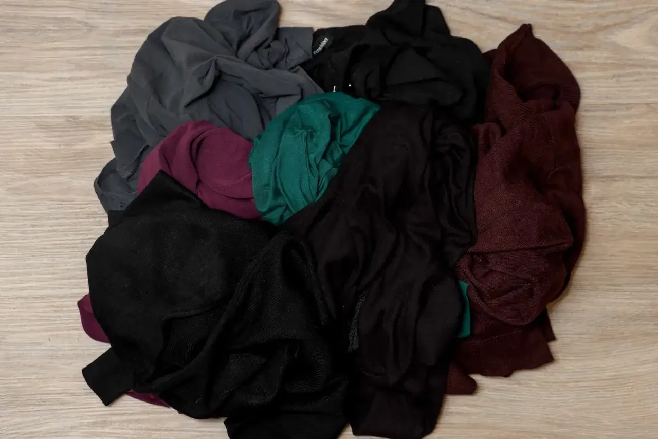 Een hoop donkere kleding, waaronder zwarte, grijze, bordeauxrode en groene items, klaar voor de donkere handdoeken wassen.