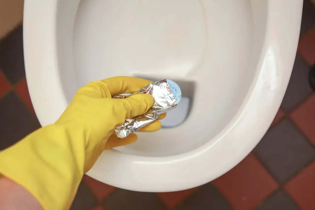 Gele handschoen houdt product vast om kalkrand wc pot verwijderen.