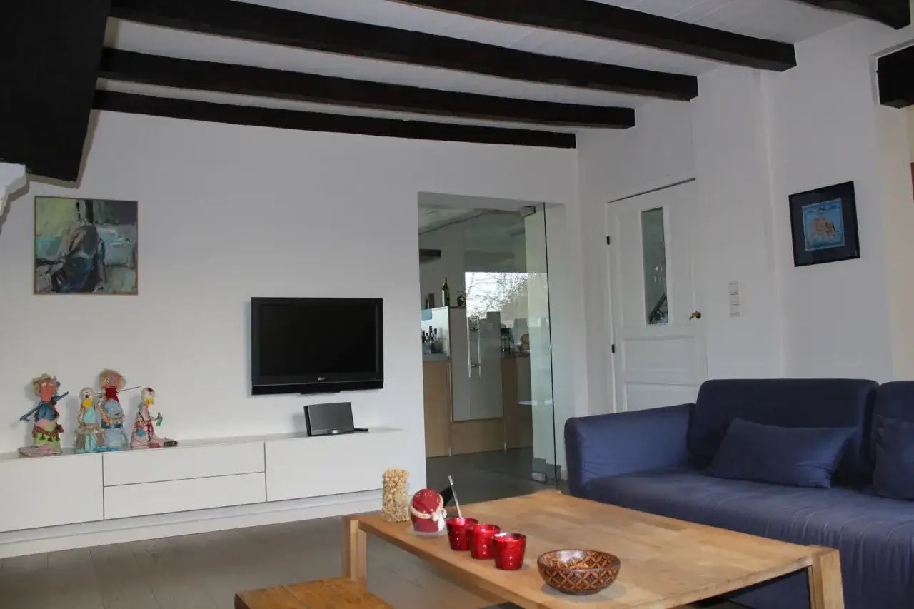 Donkere balken plafond schilderen met witte kleur voor een modern effect. Een gezellige woonkamer met blauwe bank.