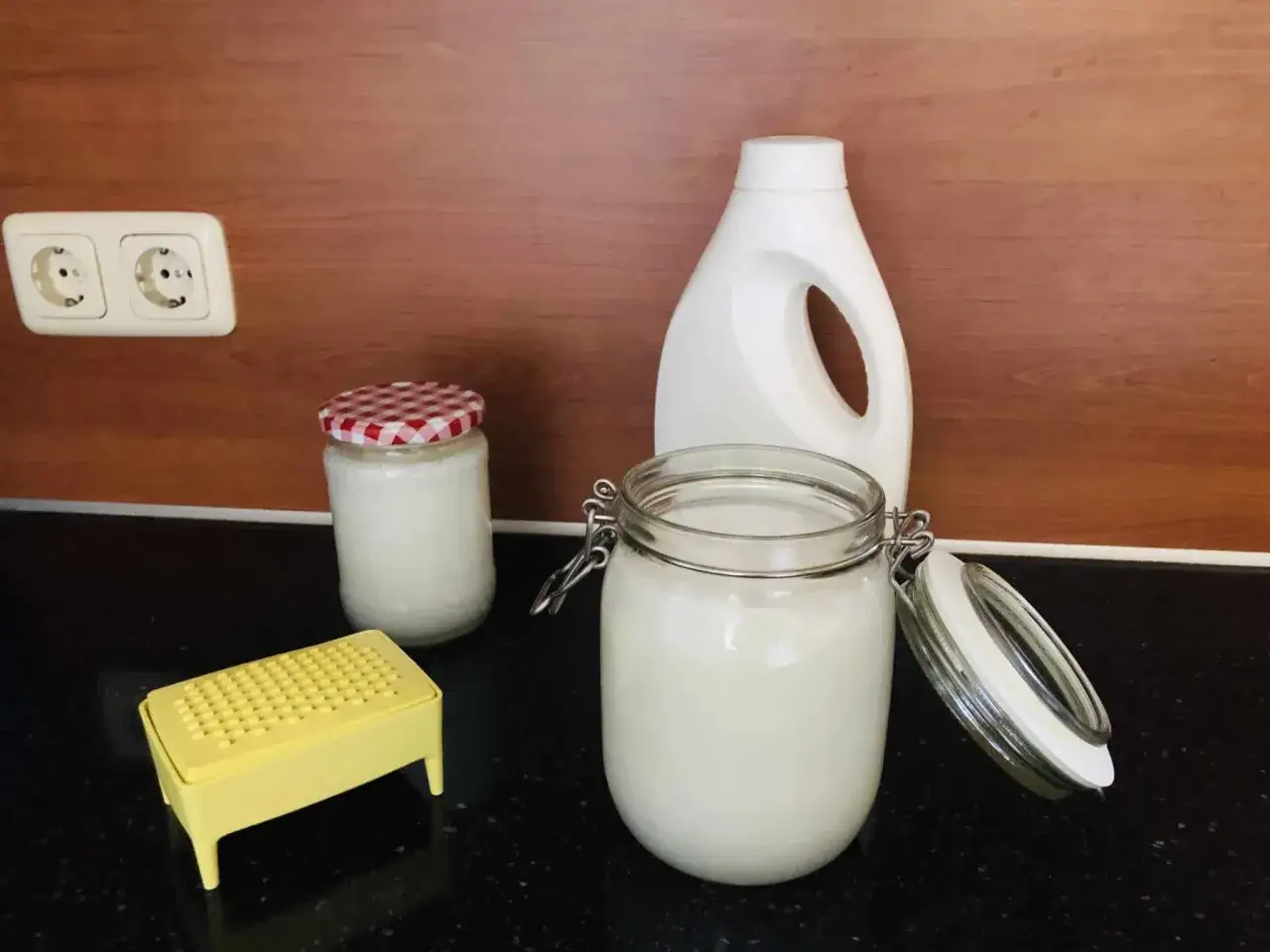 Zelf wasmiddel maken ervaringen: potten met zelfgemaakt wasmiddel, een lege fles en een gele rasp staan klaar.