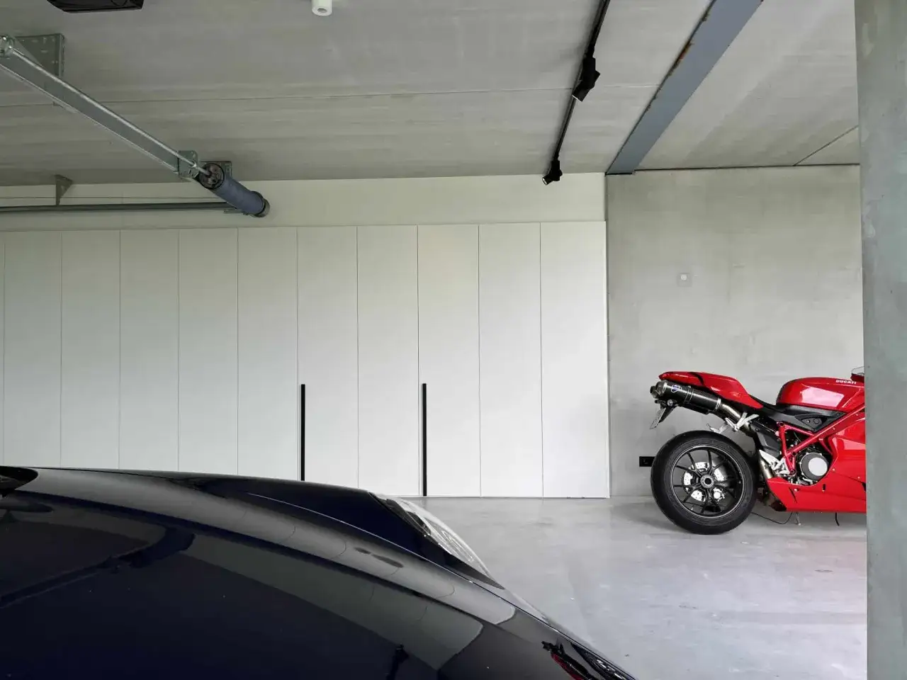 Moderne garage met witte kastenwand, een rode motor en een donkere auto. Inspiratie voor garage ideeen.