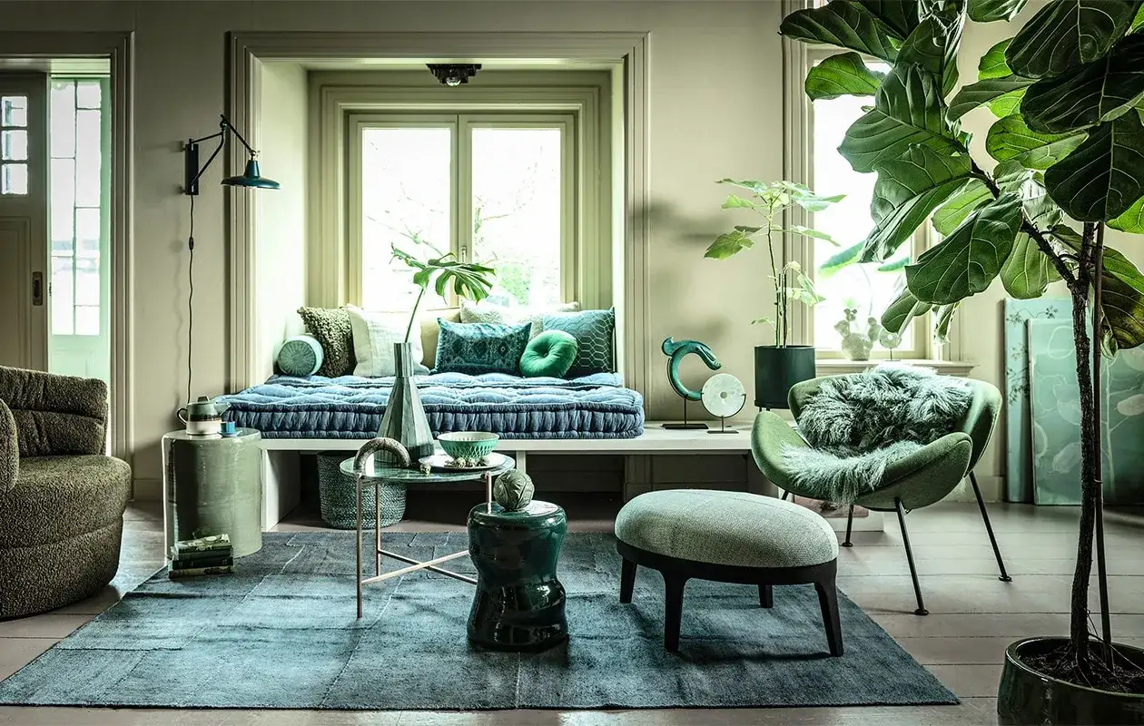 Groene bank met blauwe kussens, een groene fauteuil met vacht, en een vloerkleed. Welke kleur past bij groene bank? Blauw en grijs!