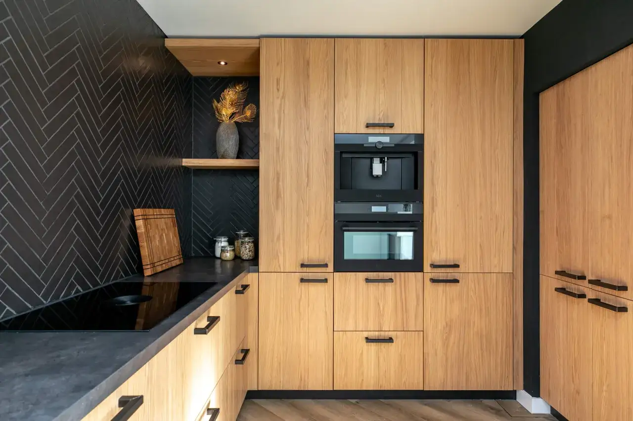 Moderne keuken met houten kasten en een houten vloer. Zwarte visgraat tegels op de achterwand en een inductiekookplaat.