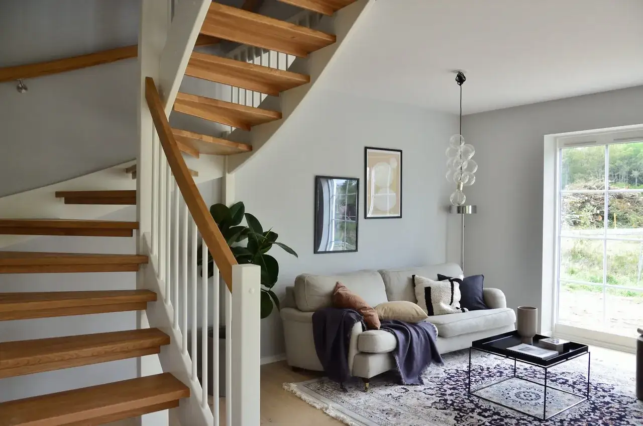 Moderne woonkamer met houten trap. Inspiratie voor trap bekleden: strakke lijnen, lichte kleuren en planten.