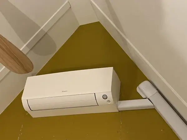 Een witte airco unit met een Daikin logo, netjes gemonteerd. De airco leidingen zijn weggewerkt in witte kokers, wat zorgt voor een strakke afwerking.