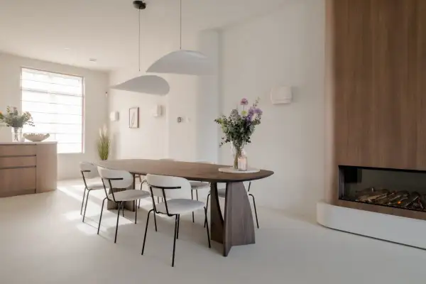 Eettafel met stoelen in een modern, licht interieur. Een vaas met bloemen en een kaars op tafel. Een gashaard met houten ombouw. Dit feng shui huis straalt rust uit.