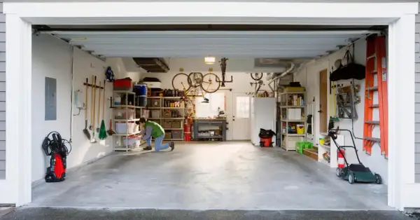 Een man richt een kleine garage in. Fietsen hangen aan het plafond, gereedschap hangt aan de muur en er staan opbergkasten vol spullen.