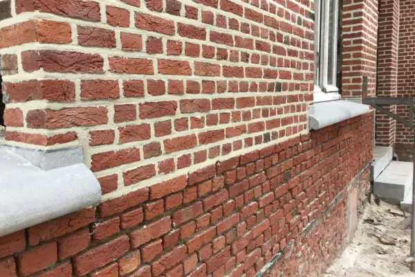 Gedetailleerd zicht op een nieuwe gevel plaatsen met rode bakstenen en wit voegwerk. De textuur van de stenen is duidelijk zichtbaar.