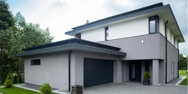 Moderne woning met grijze buiten stuc, donkere garagepoort en entree. Omringd door groen.