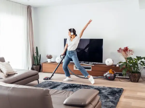 Vrolijke vrouw met koptelefoon danst tijdens de voorjaarsschoonmaak met de stofzuiger.
