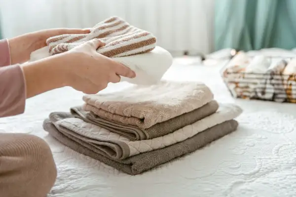 Handen vouwen gestreepte en effen handdoeken. De stapel handdoeken op het bed is zo netjes, dat ze bijna niet drogen.