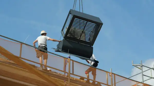 Bouwvakkers plaatsen een grote, prefab ventilatie-unit op een dak. Dit laat zien hoe wat is prefab: kant-en-klare onderdelen die snel gemonteerd worden.