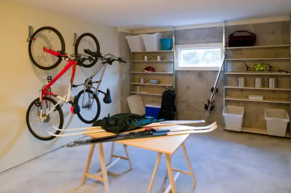 Een opgeruimde kelder met fietsen aan de muur, ski's op een tafel en opbergplanken vol spullen.