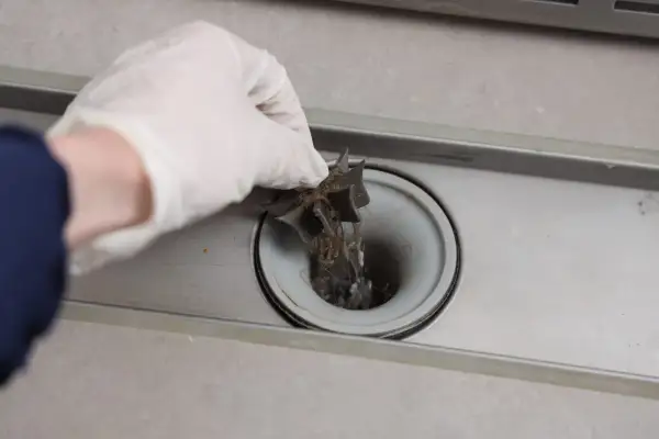 Hand met handschoen trekt haren uit een verstopt doucheputje.