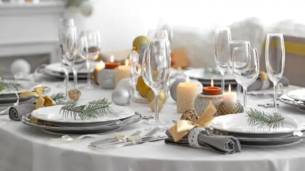 Een feestelijk gedekte tafel met glazen, kaarsen, kerstballen en dennentakjes. Klaar voor een gezellig diner!