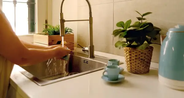 Iemand is bezig met het wasbak keuken schoonmaken. Water stroomt uit de kraan terwijl de handen een spons vasthouden.
