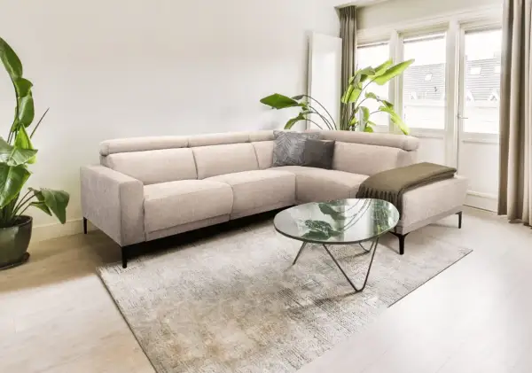 Licht beige hoekbank met kussens en plaid, een marmeren salontafel en grote planten creëren een rustig slow living interieur.