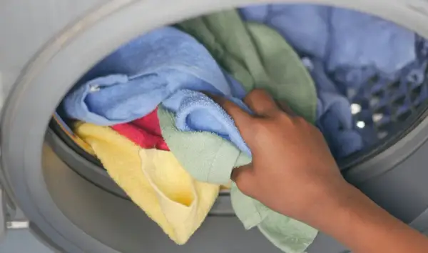 Hand pakt kleurrijke handdoeken en ondergoed uit de wasmachine.