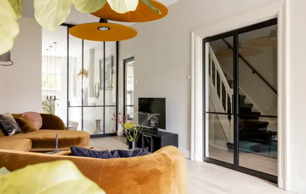 Luxe vestibule woning met oranje bank, glazen deuren naar de trap en een tv-hoek.