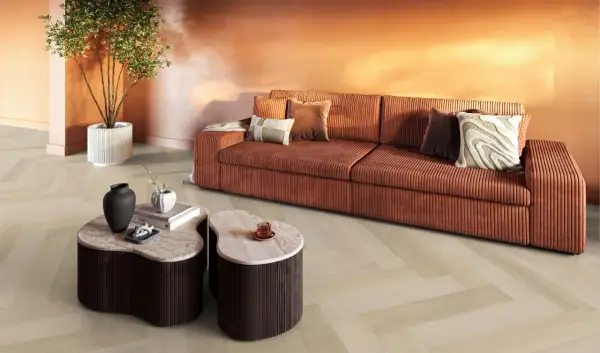 Een woonkamer met een oranje bank, marmeren tafels en een plant. De lichte evc vloer met visgraatmotief vormt een rustige basis.