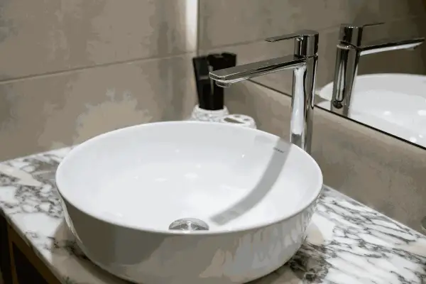 Moderne witte wasbak met een glanzende kraan. Er zijn lichte krassen in de wasbak te zien, die het dagelijks gebruik verraden.