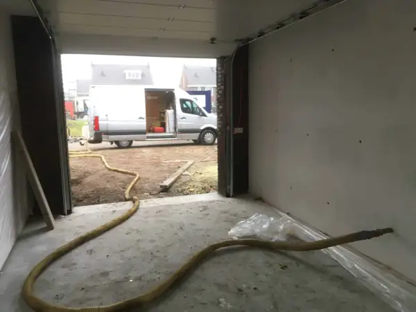 Grote gele slang voor zand stralen in een garage, met een busje buiten.