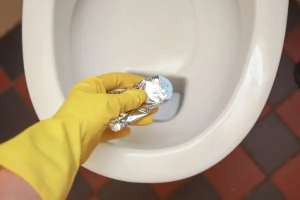 Gele handschoen houdt product vast om kalkrand wc pot te verwijderen.