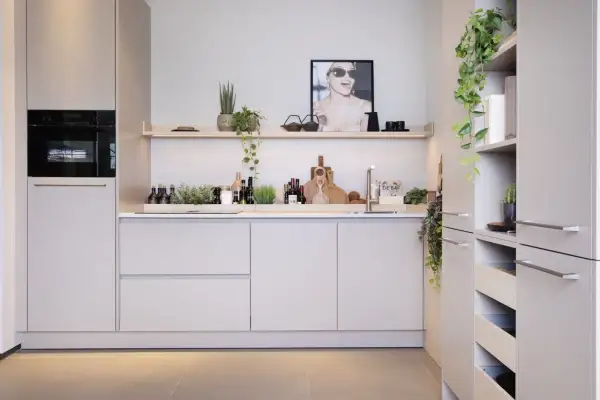 Moderne nis keuken met ingebouwde oven, strakke kasten en decoratieve planten. Een poster met een lachende vrouw siert de muur.