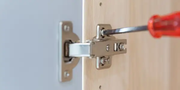 Met een schroevendraaier worden twee schroeven van een scharnier bijgesteld om de kastdeur perfect te laten sluiten.