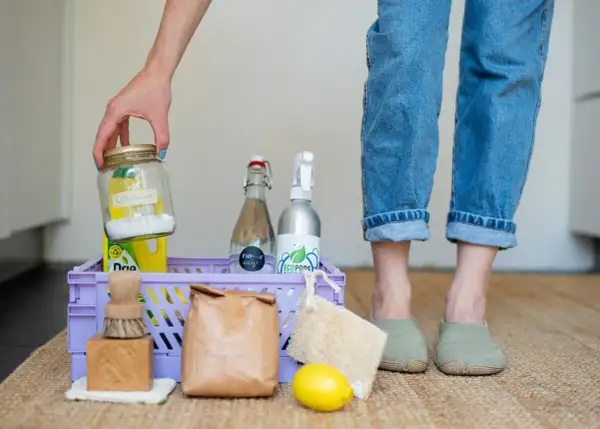 Een mand met spullen voor duurzaam schoonmaken: citroenzuur, azijn, zeep, borstel, citroen en een loofah.
